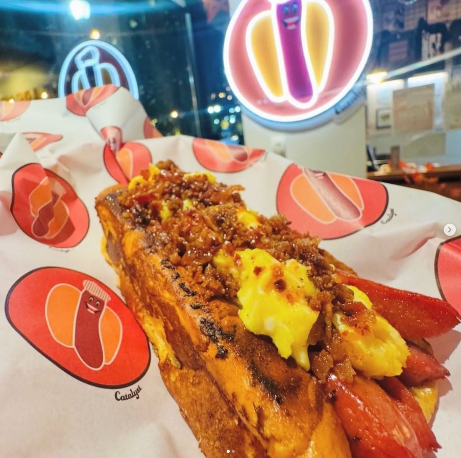 Catalyst Hot Dogs chili dog served on custom greaseproof paper with a smaller repeating hot dog logo pattern